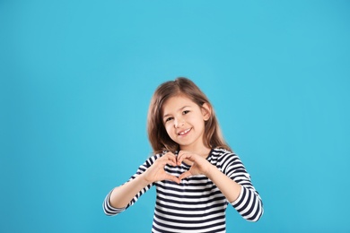 Girl making heart with her hands on color background