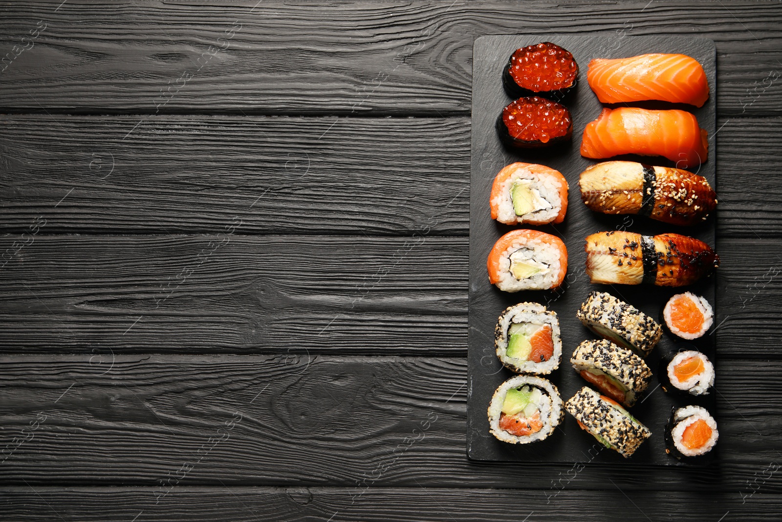 Photo of Set of delicious sushi rolls on black wooden table, top view. Space for text