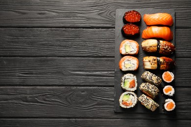 Set of delicious sushi rolls on black wooden table, top view. Space for text