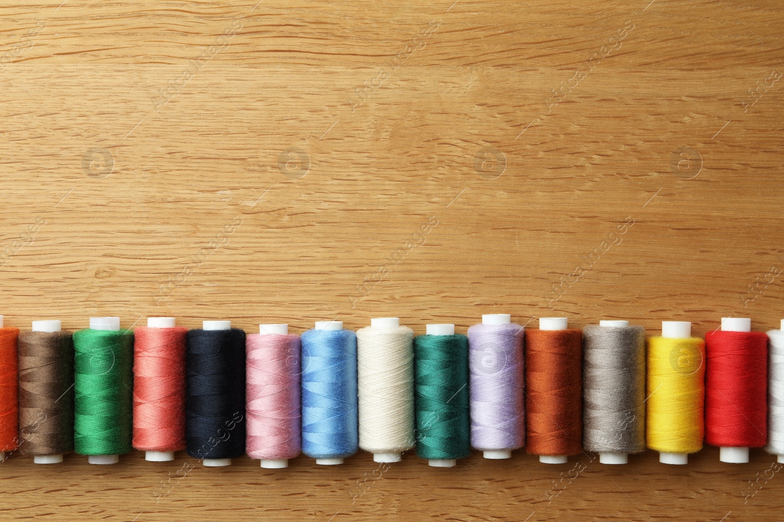 Photo of Many colorful sewing threads on wooden table, flat lay. Space for text