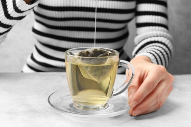 Photo of Tea brewing. Woman putting tea bag into cup at light table, closeup