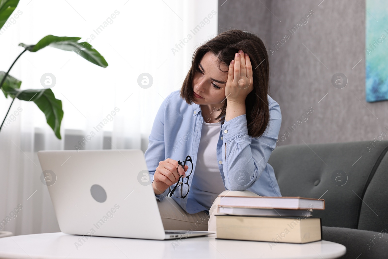 Photo of Overwhelmed woman with glasses sitting on sofa indoors