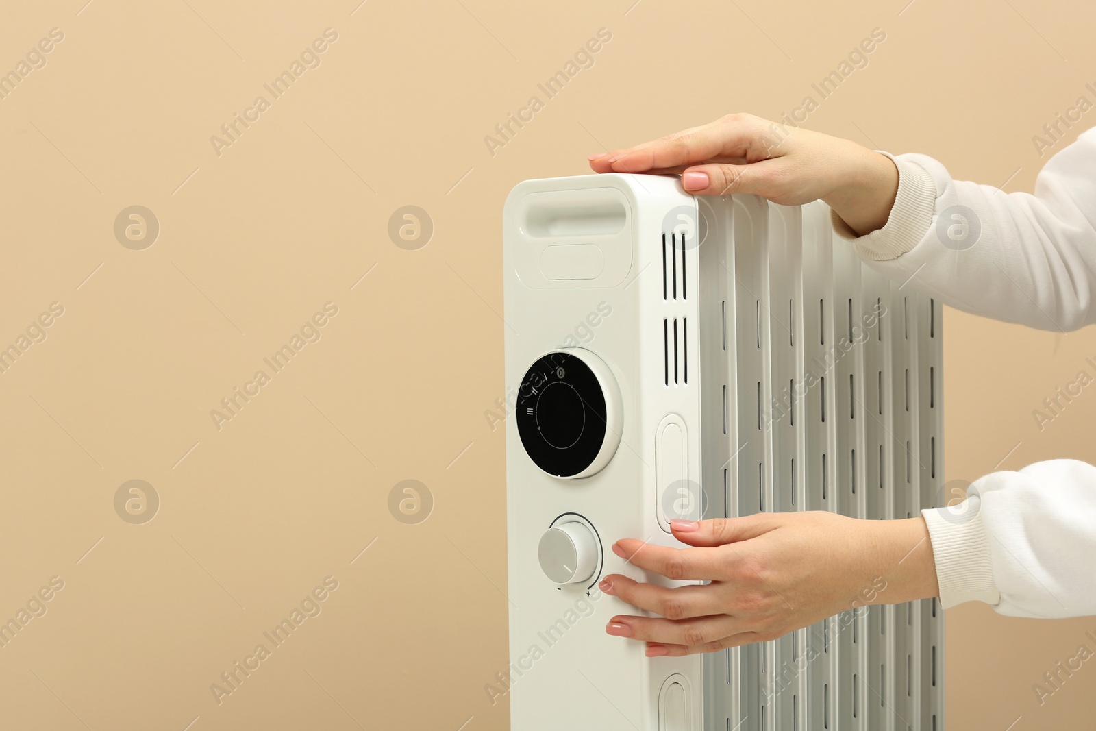 Photo of Young woman adjusting temperature on modern electric heater against beige background, closeup. Space for text