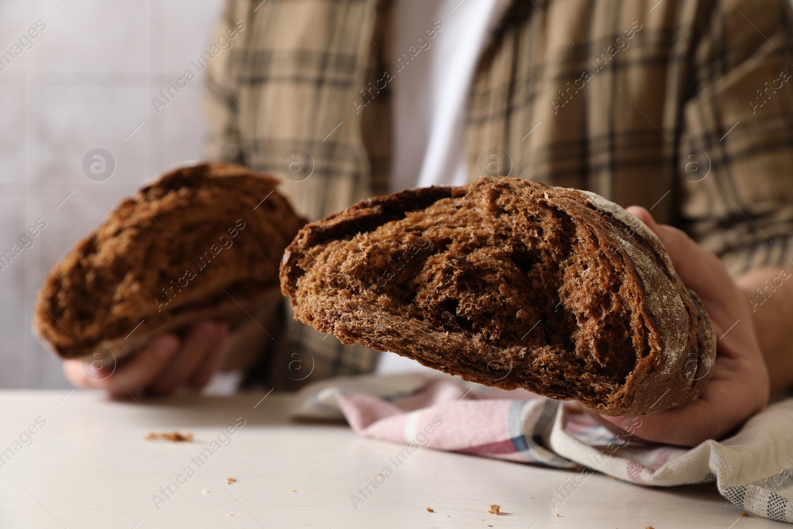 Photo of Man holding loaf of fresh broken bread on white table, closeup