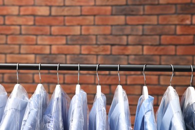 Photo of Dry-cleaning service. Many different clothes hanging on rack against brick wall, space for text