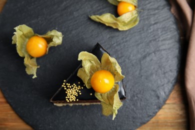 Photo of Piece of tasty cake decorated with physalis fruit on wooden table, top view