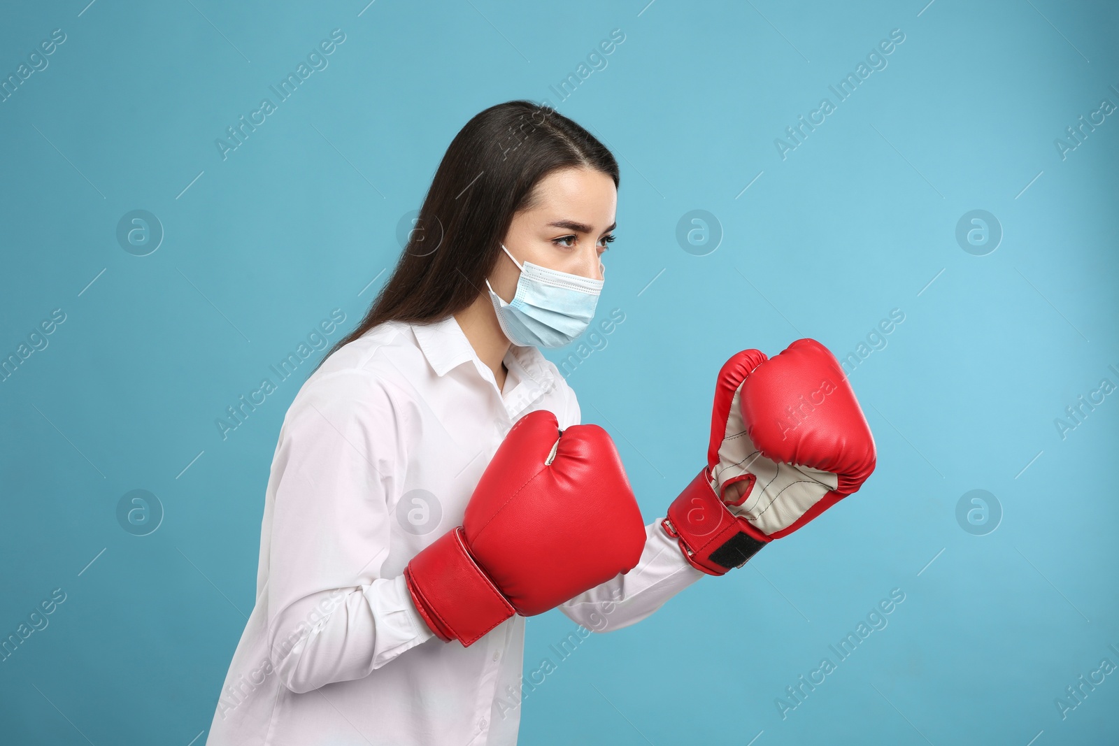 Photo of Woman with protective mask and boxing gloves on light blue background. Strong immunity concept