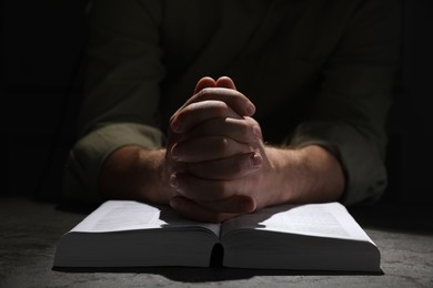 Photo of Religion. Christian man praying over Bible at table, closeup