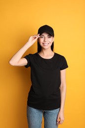 Photo of Young happy woman in black cap and tshirt on yellow background. Mockup for design