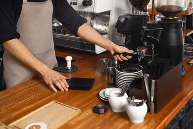 Photo of Barista pouring milled coffee from grinding machine into portafilter at bar counter, closeup