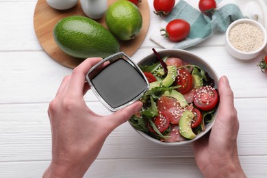 Woman adding soy sauce to tasty salad at white wooden table, closeup