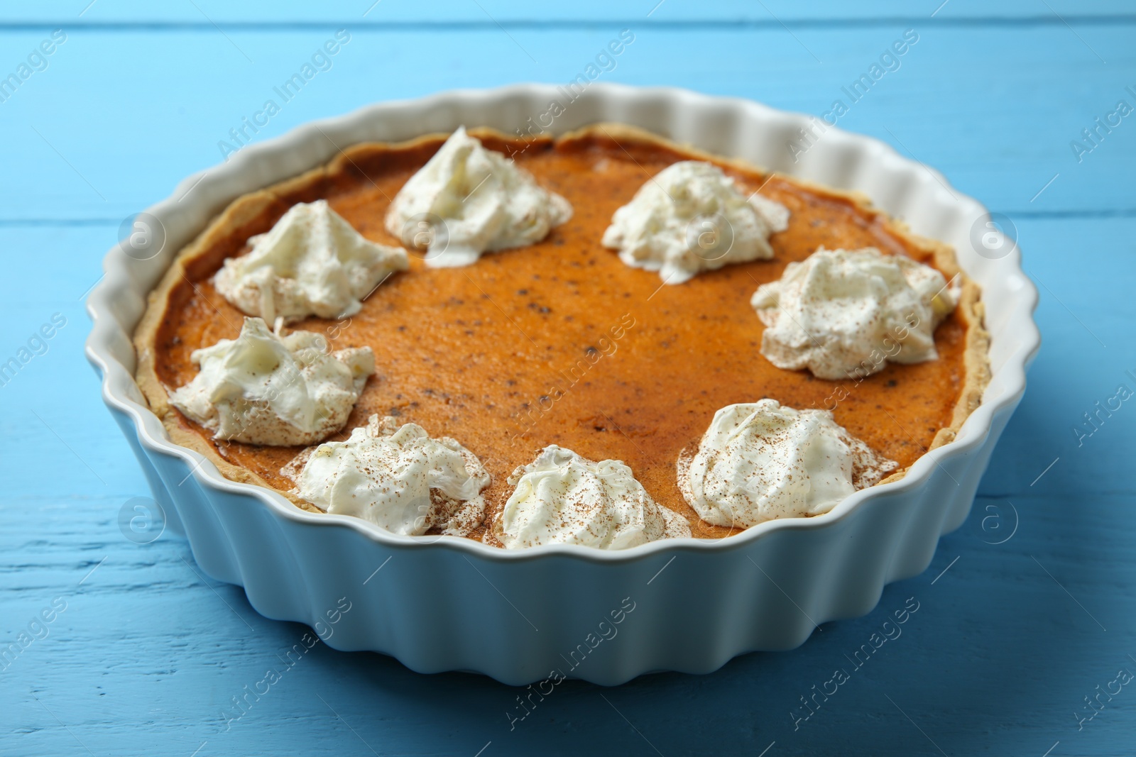 Photo of Delicious pumpkin pie with whipped cream on light blue wooden table, closeup