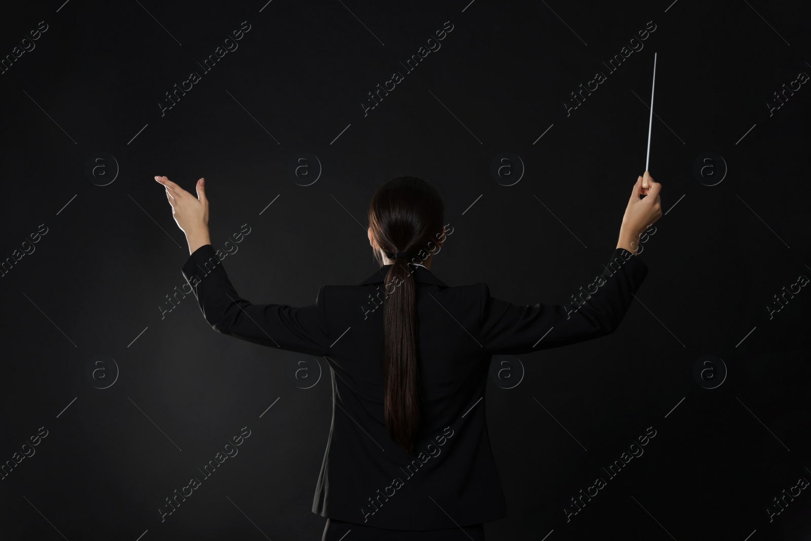 Photo of Professional conductor with baton on dark background, back view