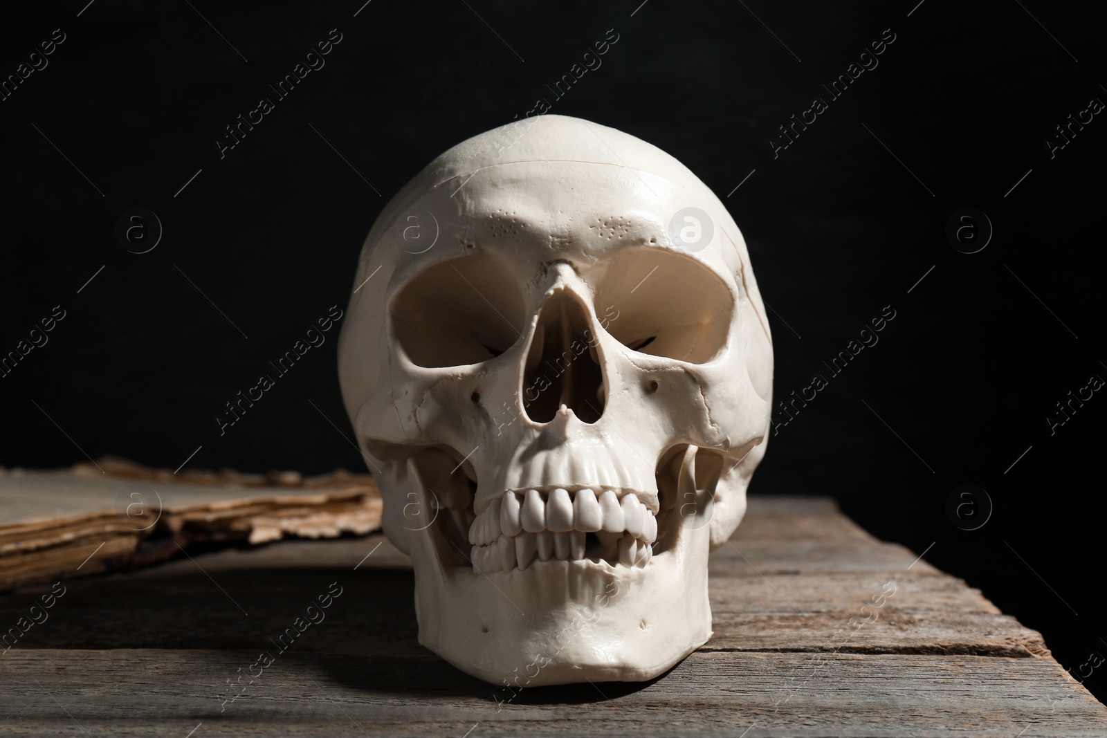 Photo of Human skull and old book on wooden table against black background