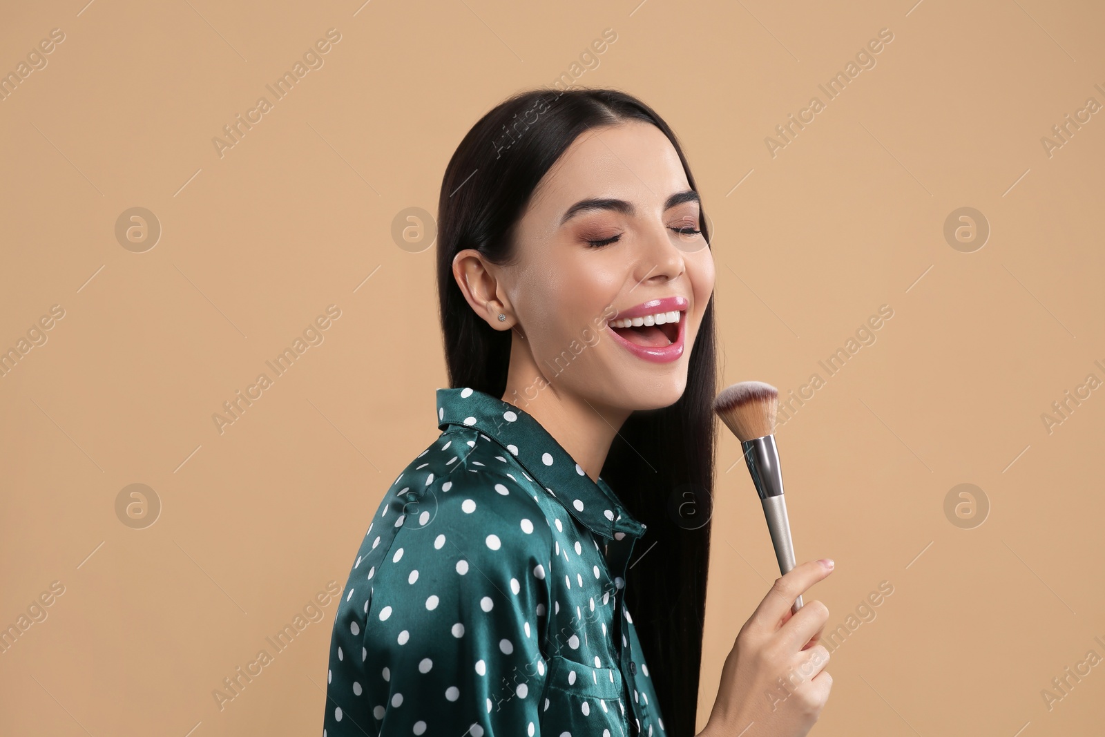 Photo of Happy woman with makeup brush on light brown background