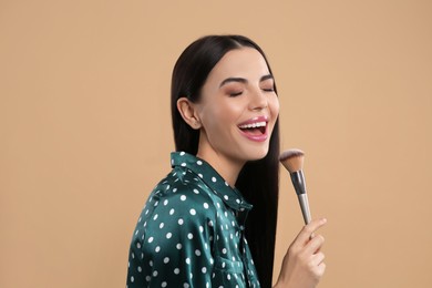 Photo of Happy woman with makeup brush on light brown background