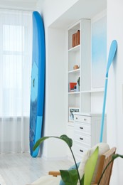 Photo of SUP board, paddle and stylish shelving unit in room. Interior design