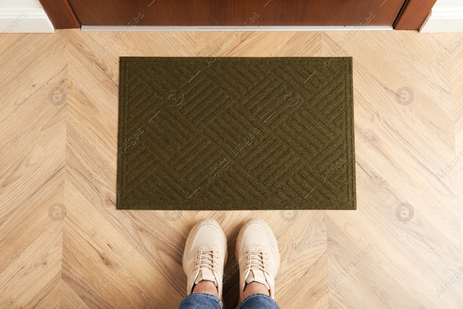 Photo of Woman standing near door mat on wooden floor in hall, top view