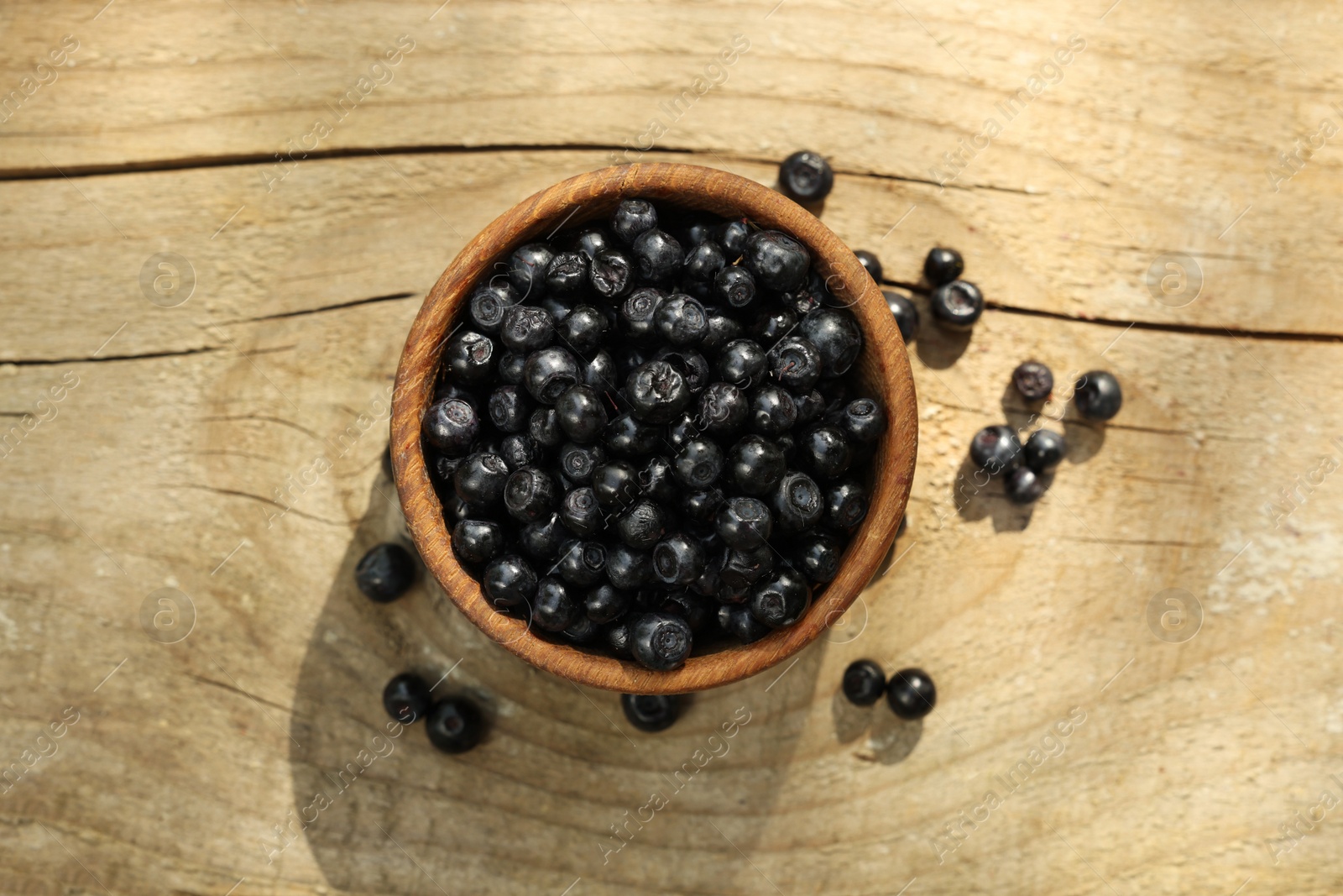 Photo of Bowl of fresh bilberries on wooden table, top view