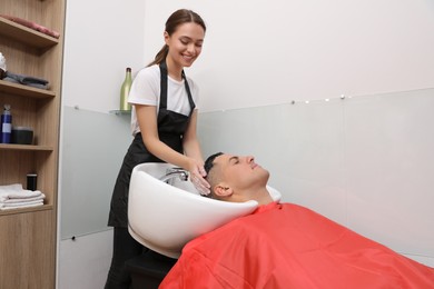 Professional hairdresser washing client's hair at sink in salon