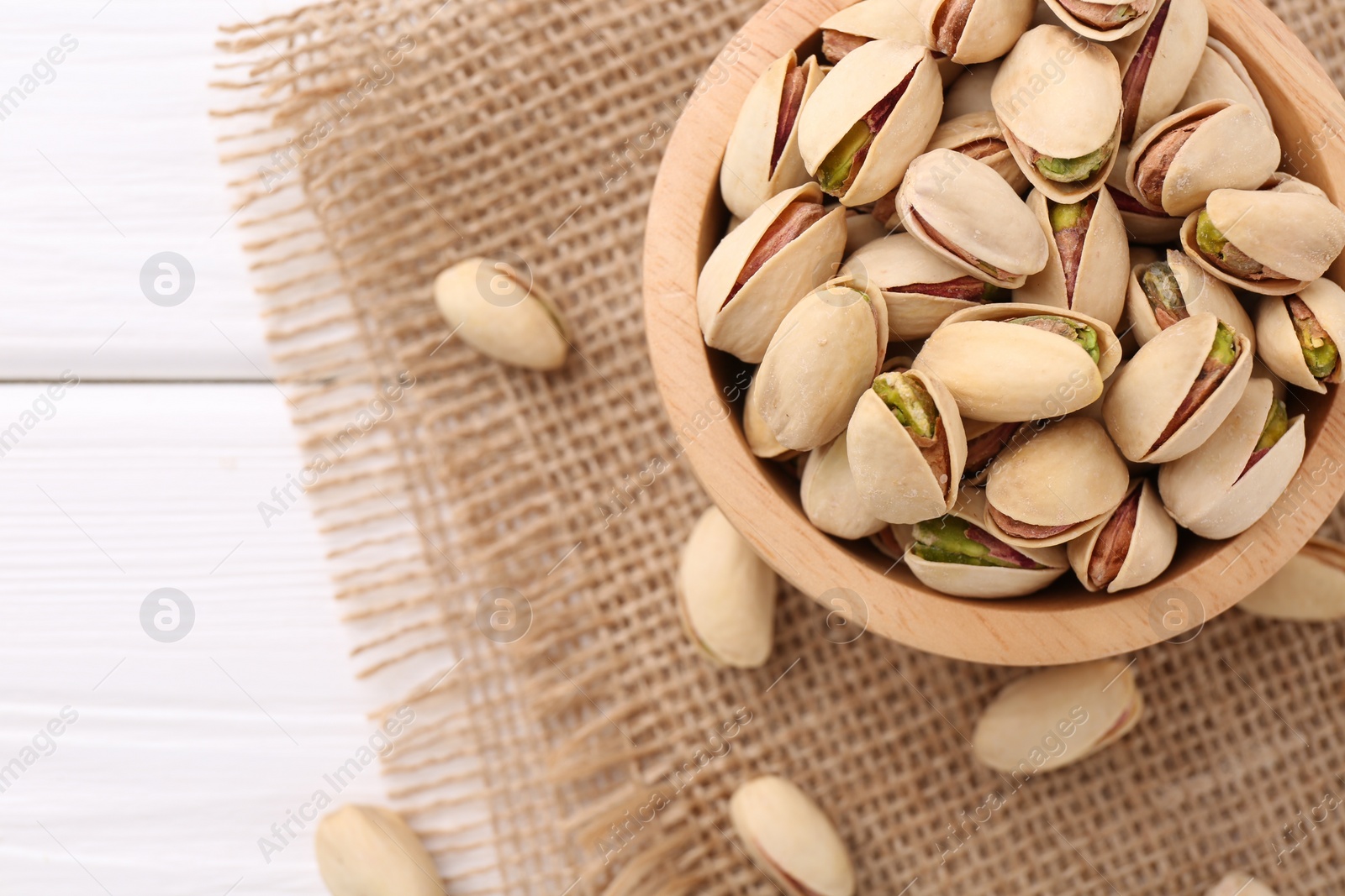 Photo of Tasty pistachios in bowl on white wooden table, top view. Space for text