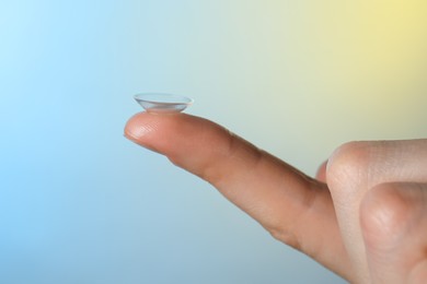 Photo of Woman holding contact lens on color background, closeup