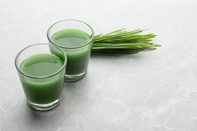 Photo of Glasses of wheat grass juice and green sprouts on marble table. Space for text