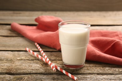 Photo of One glass of tasty milk, straws and napkin on wooden table