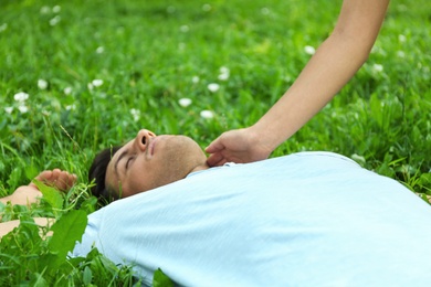 Photo of Woman checking pulse of unconscious man outdoors. First aid
