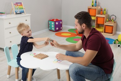 Photo of Motor skills development. Happy father helping his son to play with geoboard and rubber bands at white table in room
