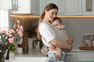 Mother holding her child in sling (baby carrier) in kitchen