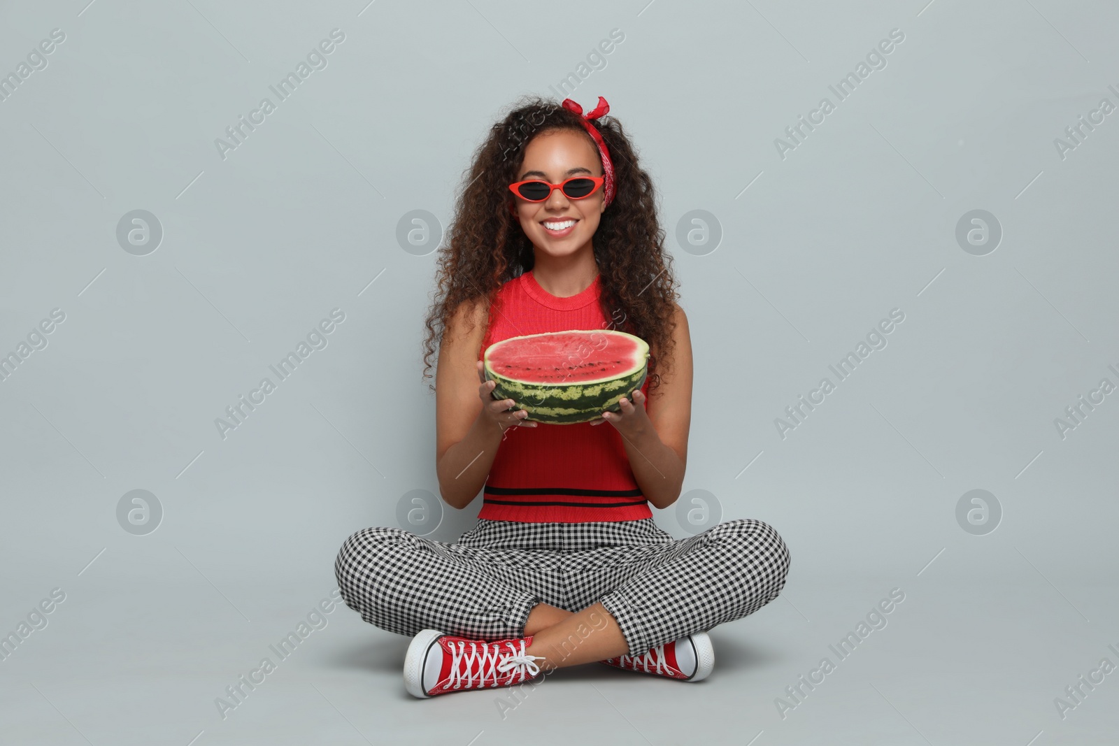 Photo of Beautiful young African American woman with half of watermelon on grey background