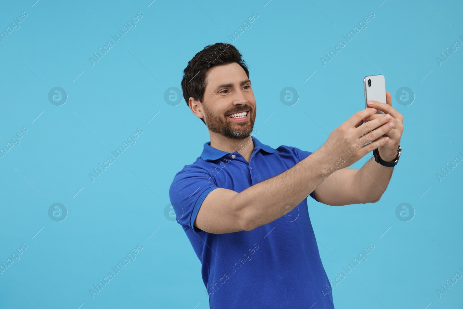 Photo of Smiling man taking selfie with smartphone on light blue background, space for text