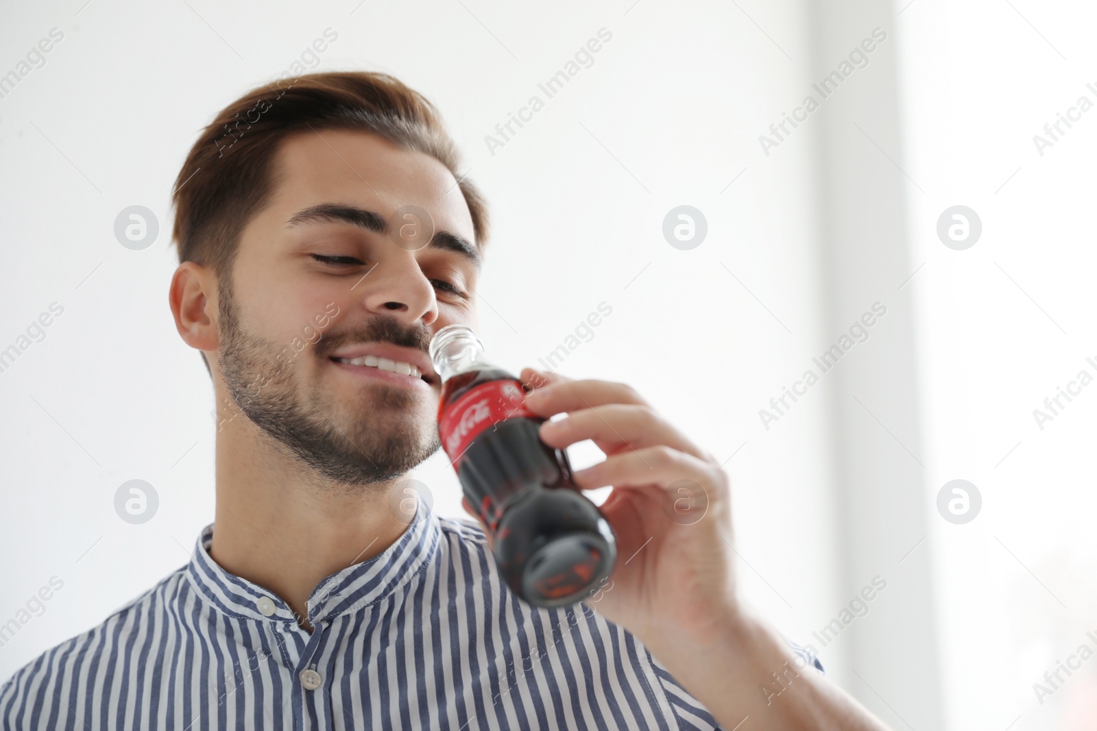 Photo of MYKOLAIV, UKRAINE - NOVEMBER 28, 2018: Young man with bottle of Coca-Cola indoors, space for text