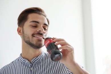 Photo of MYKOLAIV, UKRAINE - NOVEMBER 28, 2018: Young man with bottle of Coca-Cola indoors, space for text