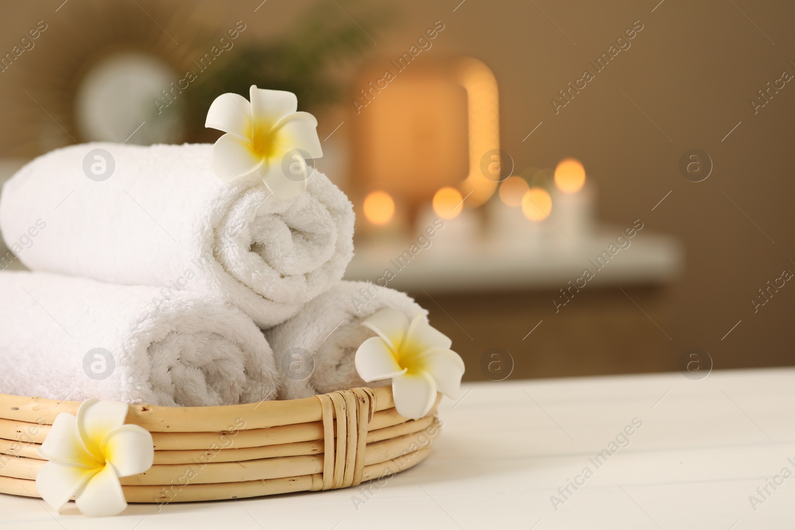 Photo of Spa composition. Rolled towels and plumeria flowers on white table indoors. Space for text