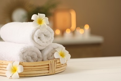 Photo of Spa composition. Rolled towels and plumeria flowers on white table indoors. Space for text