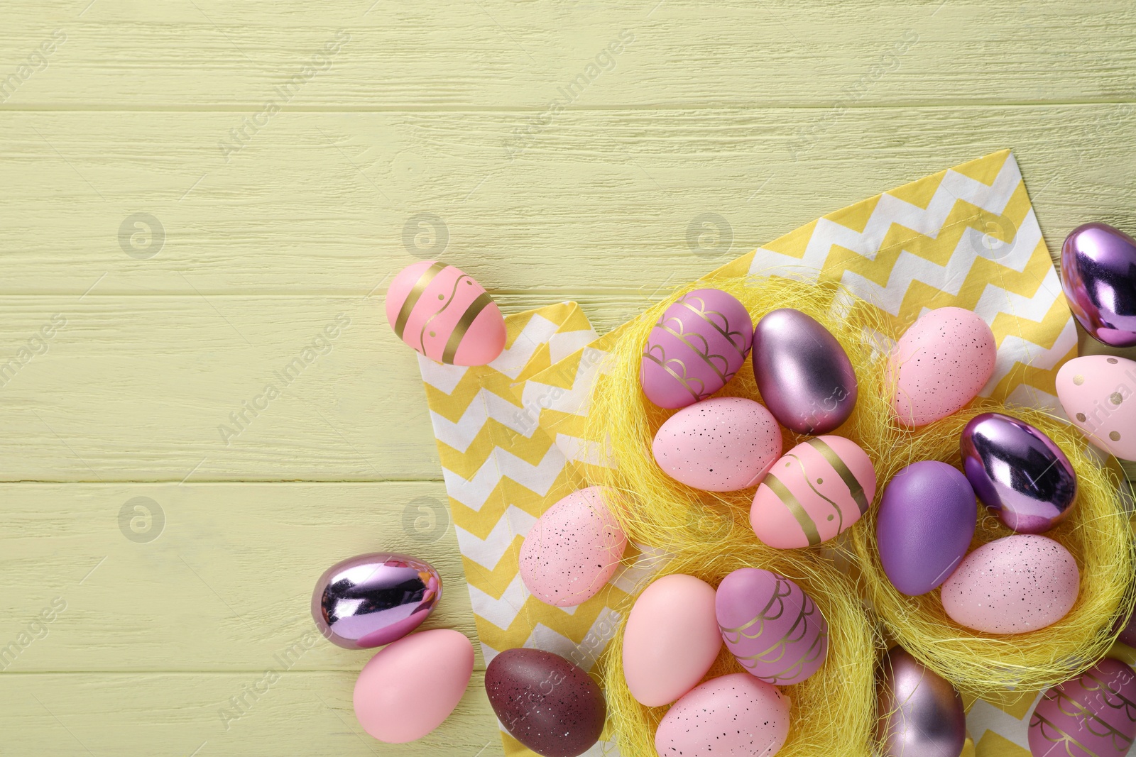 Photo of Decorative nests with many beautiful Easter eggs on yellow wooden table, flat lay