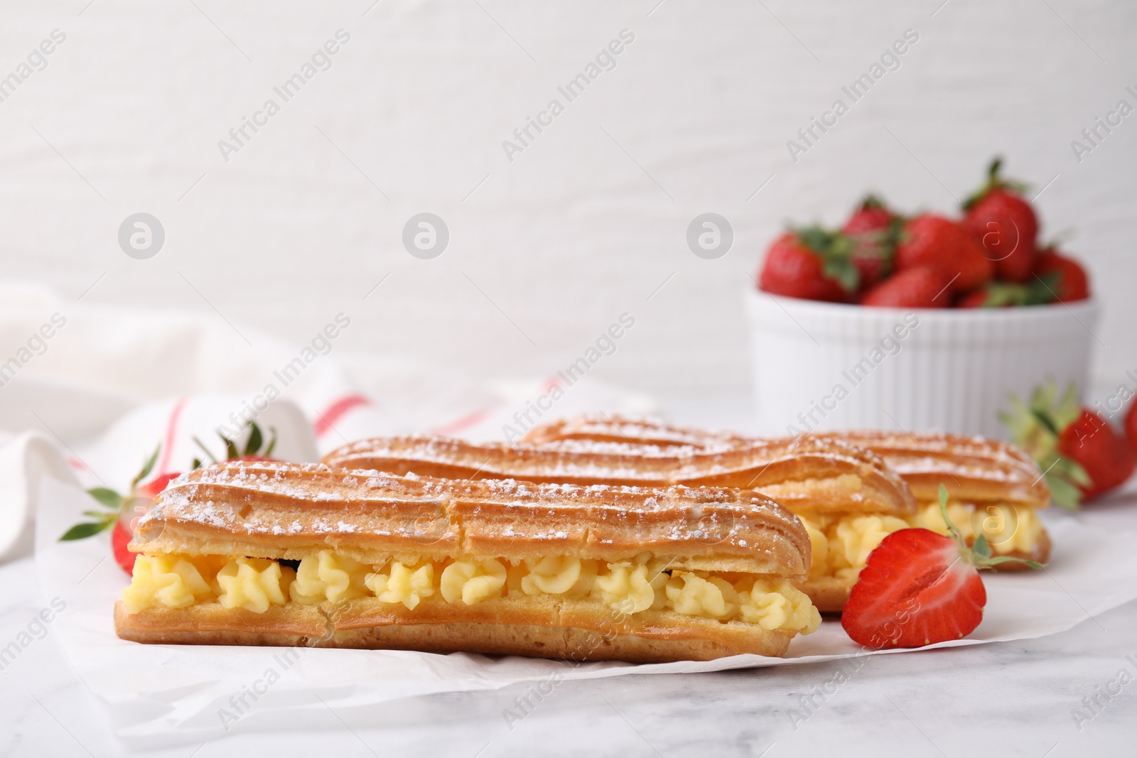 Photo of Delicious eclairs filled with cream and strawberries on white marble table