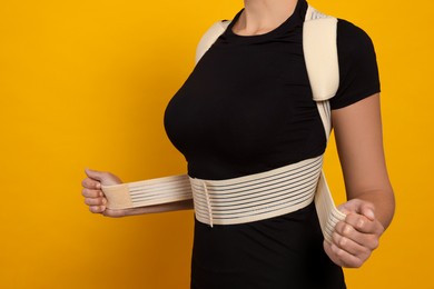 Closeup view of woman with orthopedic corset on orange background. Space for text