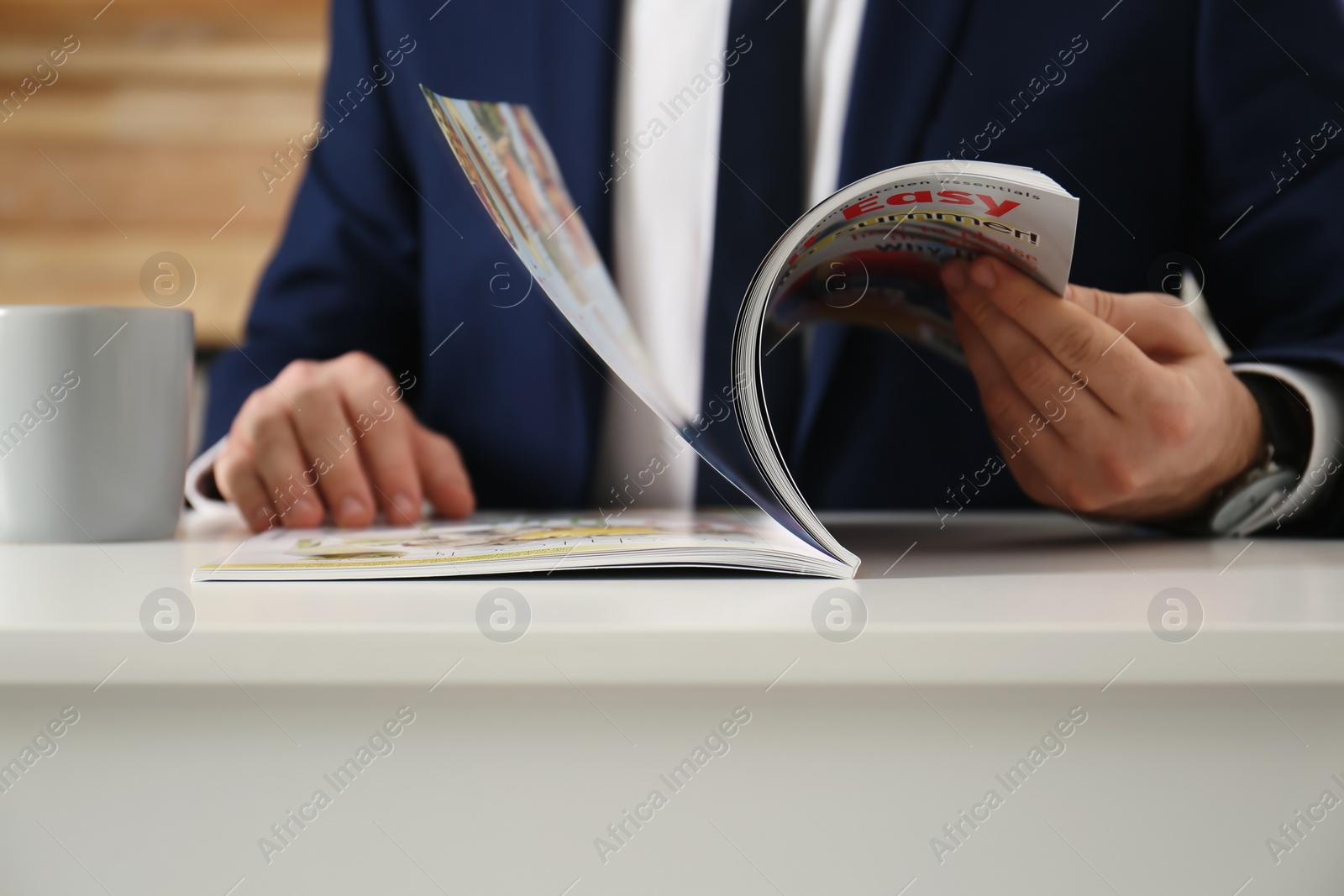 Photo of Businessman reading modern magazine at table indoors, closeup