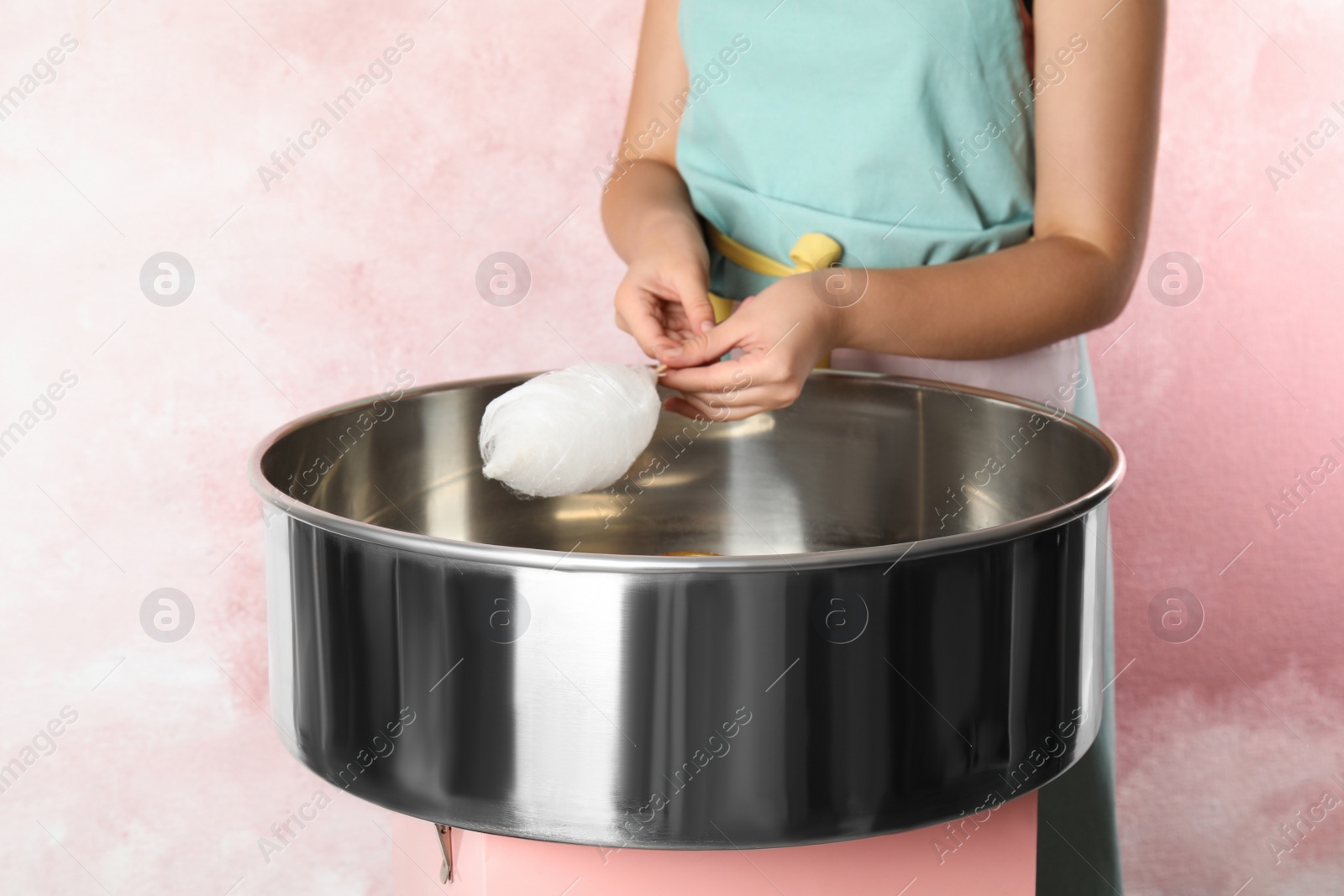 Photo of Young woman making cotton candy with modern machine on pink background, closeup