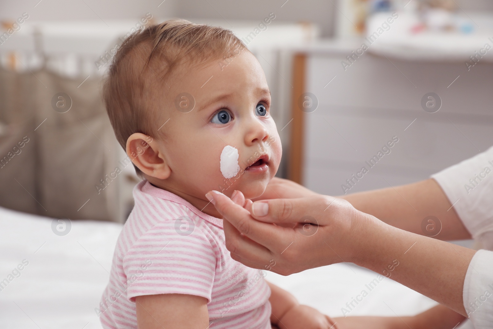 Photo of Mother applying moisturizing cream on her little baby at home, closeup