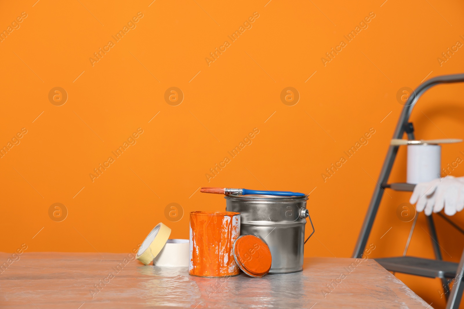 Photo of Can with paint, brush and renovation equipment on table against orange background. Space for text