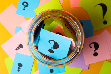 Photo of Colorful cards with question marks and glass jar on yellow background, top view