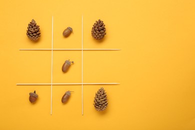 Photo of Tic tac toe game made with acorns and pine cones on yellow background, top view. Space for text