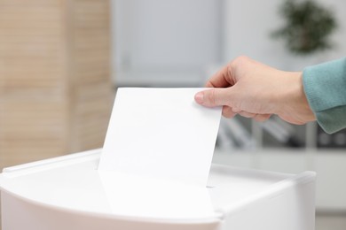 Photo of Woman putting her vote into ballot box on blurred background, closeup