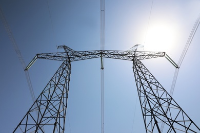 High voltage tower with electricity transmission power lines against blue sky, low angle view