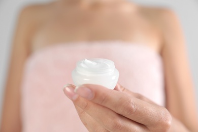 Photo of Young woman holding jar of cream on grey background, closeup