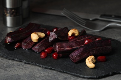 Photo of Raw cut black carrot with pomegranate seeds and cashew on grey table, closeup
